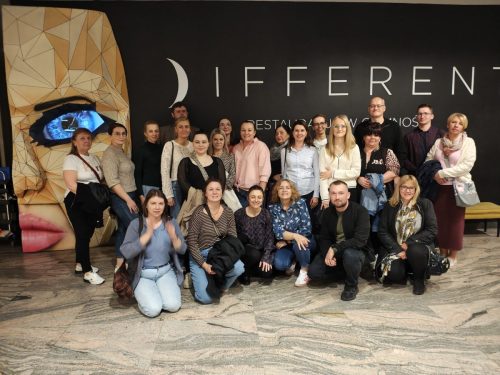 Grupowe zdjęcie na tle dużego banera z napisem DIFFEREN. Osoby w pierwszym rzędzie klęczą.