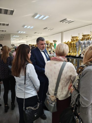 Grupa osób w pomieszczeniu z złotymi i srebrnymi pucharami.