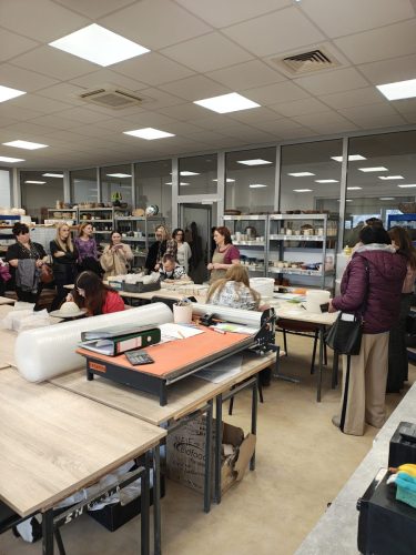 Grupa osób oprowadzana po pracowni w której są wytwarzane między innymi kubki.