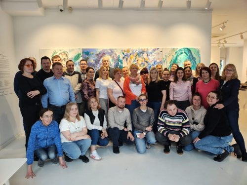 Grupowe zdjęcie na tle obrazów. Osoby w pierwszym rzędzie klęczą.