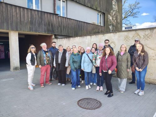 Grupowe zdjęcie na zewnątrz, na tle budynku z drewnianą elewacją.