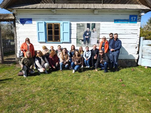 Grupowe zdjęcie na tle starego, drewnianego, białego domu.