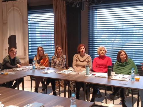 Sześć kobiet siedzi obok siebie przy stole konferencyjnym i patrzy w jednym kierunku.