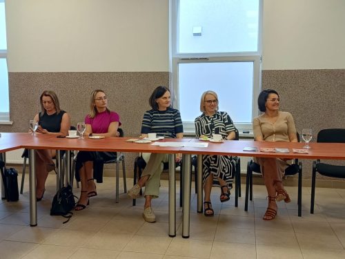 Podłużny stół przy którym siedzi 5 kobiet i patrzy w jednym kierunku.