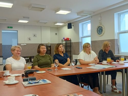Sala z stołami połączonymi w kształt litery L przy którym siedzi 5 kobiet.