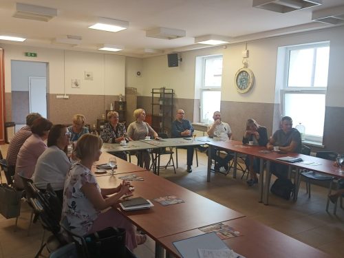 Sala z łączonymi stołami w kształt litery U przy których siedzą uczestnicy.
