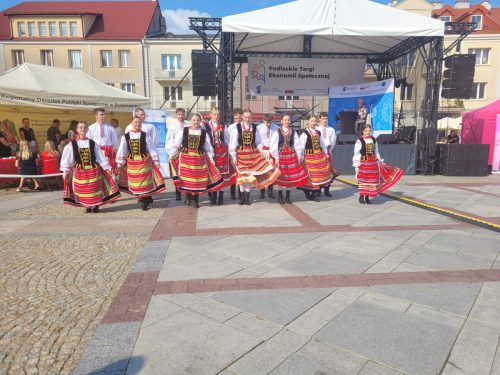 Rynek Kościuszki w Białymstoku na nim znajduję się zespół tańca ludowego, osoby z zespołu są przebrane w ludowe stroje oraz wykonują występ taneczny.