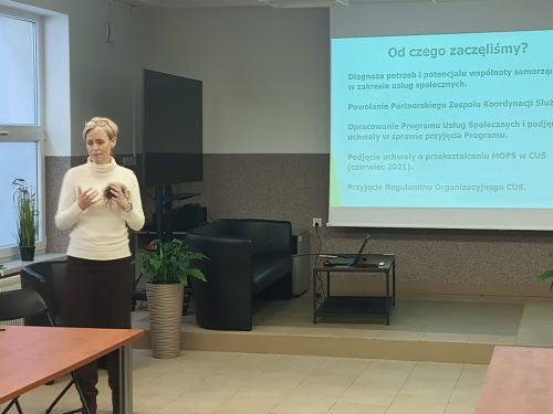 Kobieta przemawia stojąc z boku ekranu projekcyjnego na którym jest wyświetlona prezentacja.