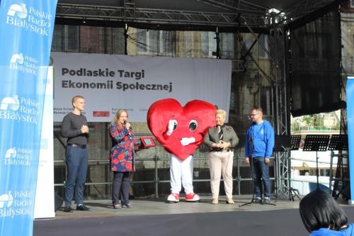scena targów ekonomii społecznej na niej prezenter tłumacz migowy maskotka targów Dyrektor Rajewska-Nikonowicz Dyrektor Tomaszewska oraz patronat medialny Polskie radio Białystok oddział w Białymstoku