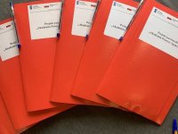 Sześć czerwonych teczek z długopisami oklejone naklejkami - Projekt partnerski Akademia Pomocy Społecznej