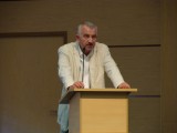 Mężczyzna ubrany na biało stoi przy mównicy i przemawia przez mikrofon.