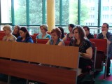 Publiczność siedzi w ławkach w kilku rzędach na sali wykładowej.