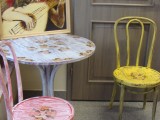 Kolorowe meble ze wzorami (dwa krzesła i stolik) stoją przy drzwiach. Na stole stoi obraz przedstawiający anioła z lutnią.