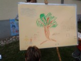 Dziecięcy rysunek narysowany na tablicy. Przedstawia drzewo, rodzinę oraz dom.