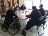 Grupa osób z czego jedna na wózku inwalidzkim siedzą przy stole i rozmawiają.