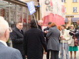 Grupa rozmawiających ze sobą ludzi. Jeden z nich trzyma niebieski znak.