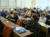 Grupa osób siedzi w ławkach podczas konferencji.
