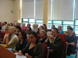 Grupa osób siedzi w ławkach podczas trwania konferencji.