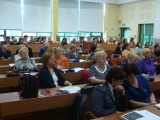 Grupa osób siedzi w ławkach podczas trwania konferencji.