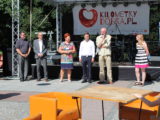Sześć osób stoi w jednym rzędzie przy scenie. Na scenie widać sprzęt muzyczny oraz baner Kilometry Dobra.
