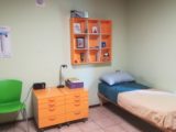 Pokój z pomarańczowymi półkami i szafkami. W rogu pokoju stoi łóżko.