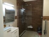 Łazienka w nowoczesnym stylu. Duża kabina prysznicowa, szafki, umywalka oraz jeszcze zafoliowane lustro.
