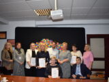 Posiedzenie Rady do Spraw Osób Niepełnosprawnych. Grupowe zdjęcie na tle logotypu Województwa Podlaskiego. Pięć osób trzyma podziękowania oprawione w ramkę.