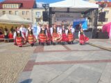 Rynek Kościuszki w Białymstoku na nim znajduję się zespół tańca ludowego, osoby z zespołu są przebrane w ludowe stroje oraz wykonują występ taneczny.