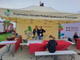 Dwie młode panie stojące przy stoisku Regionalnego Ośrodka Polityki Społecznej w Białymstoku w czasie dożynek w tle stoją wozy strażackie