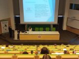 Ujęcie na uczestników i prowadzących Pana Wojciecha Mareka Depczyńskiego Prezesa Zarządu Fundacji oraz Pani Edyta Bałakier Członek Zarządu Fundacji A jak.. , na telebimie dane dotyczące diagnozy spektrum autyzmu
