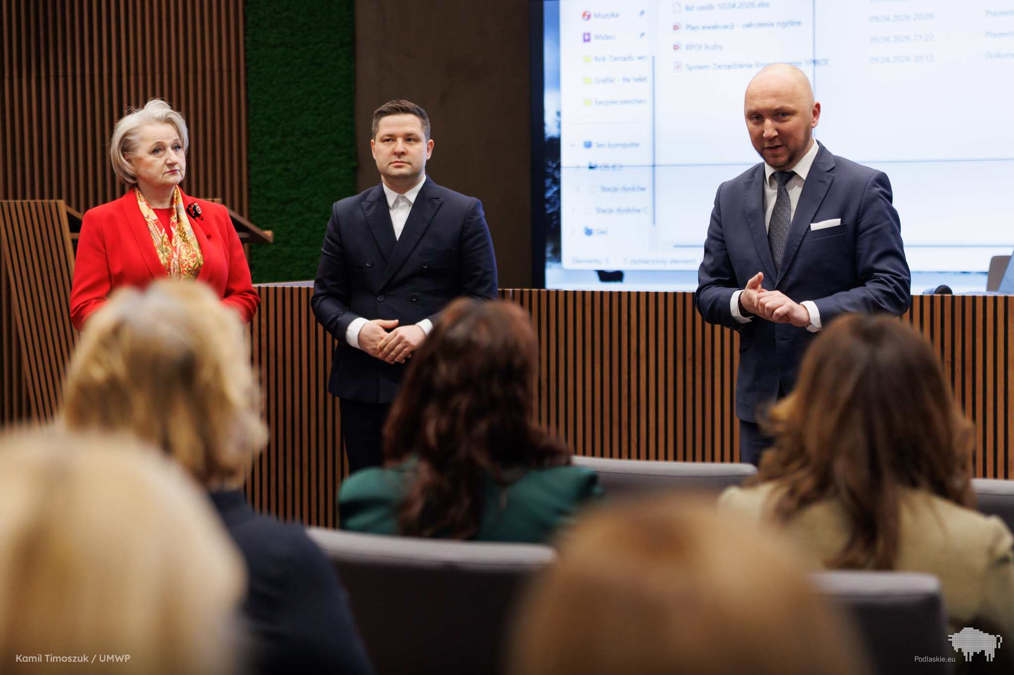 3 osoby stoją przed siedzącą publicznością są nimi od prawej Marszałek Województwa Podlaskiego Łukasz Prokorym,, następnie Prezes fundacji MY DLA INNYCH Rafał Średziński, następnie Marszałek Wiesława Burnos. W tle jest wyświetlony ekran komputera.